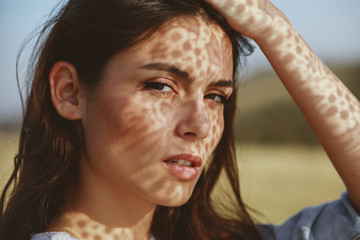 Fototapeta premium Portrait of a young woman with shadows texture on the face in a meadow with