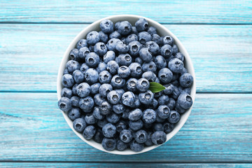 Ripe blueberries in bowl on blue wooden table