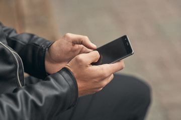 Close-up. The guy is holding a smartphone in his hands. On the street