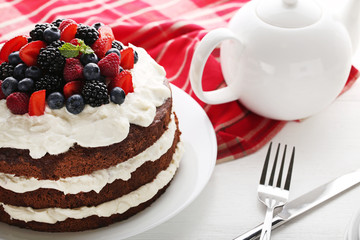 Delicious chocolate biscuit cake with berries on white wooden table