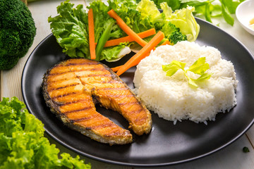 Delicious salmon steak with with rice and salads on wooden table.