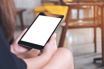 Mockup image of woman's hands holding black tablet pc with blank white screen on thigh with concrete floor background in modern cafe