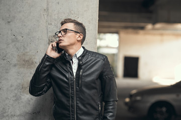 Close-up. Serious guy talking on the phone. In a leather jacket and glasses. At a construction site.