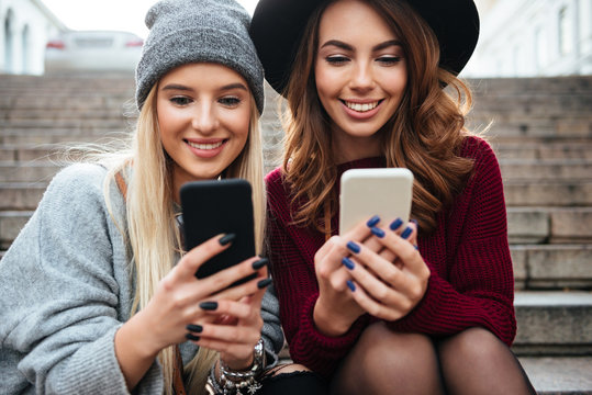 Portrait of two smiling pretty girls using mobile phones