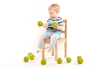 little boy sitting on a chair surrounded by apples