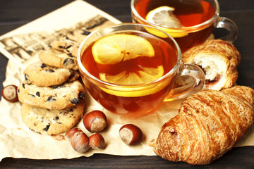  A cup of black hot tea with lemon, a biscuit with chocolate drops, hazelnut and a fresh croissant on a beige paper with vintage card postale