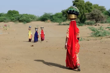 Foto op Canvas Indiase etnische vrouwen dragen een kruik op haar hoofd en gaan voor het water in een put in de woestijn. Rajasthan, India. Thar woestijn bij Jaisamler © Rafal Cichawa