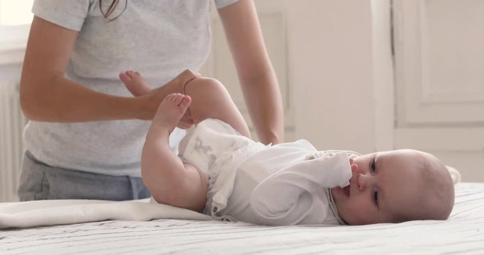 Mother putting diaper on her happy baby on bed on white background indoores