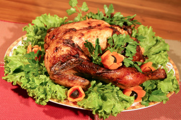 A roasted bird, decorated with green lettuce leaves, carrots and olives.