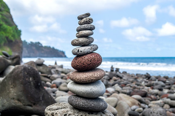 Fototapeta na wymiar Column of balanced stones on the rocky shore of the ocean on the Hawaiian island