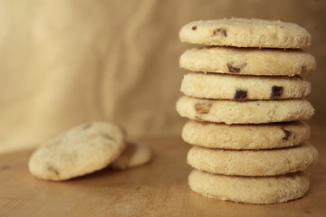 Pile or stack of choc chip and fruit cookies, on a wooden table with a neutral background. Copy space for text.