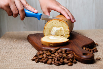 Girl's hand is cutting  roll coffee cake with knife and coffee bean on wooden cutting board
