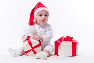 beautiful kid sitting in a New Year's cap and white body among Christmas boxes with gifts and unpacks gift