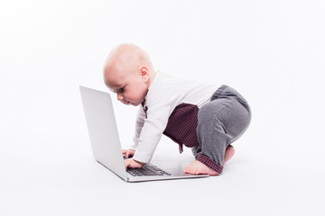 cute little baby boy sitting on a white background in front of a laptop and learns to type on it