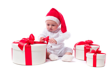beautiful kid sitting in a New Year's cap and white body among Christmas boxes with gifts and unpacks gift