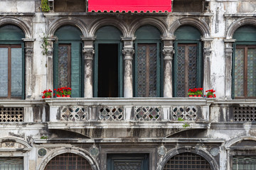 Venetian architecture. An ancient building in the Venetian style of architecture. Red flowers in red pots against the background of vintage building in Venice, Italy. Ancient balcony in Venice, Italy.