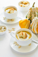 Two cups with fresh pumpkin cream soup decorated cream, seeds and crackers on white table cloth