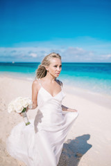 Beautiful bride in long white dress on the beach with white bouquet