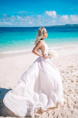 Fototapeta na wymiar Beautiful bride in long white dress on the beach with white bouquet