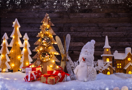 Christmas background with illuminated wooden village and snowman with tree