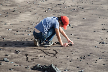 Boy drawing hearts in sand on the beach. Low tide.