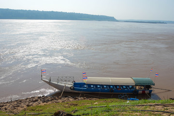 Passenger boat crossing the Thai-Laos border with the Thai flag on the Mekong River at dawn.

