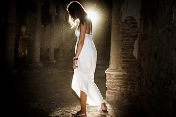Mujer con vestido blanco a contraluz en el templo antiguo iluminada por la luz del sol al atardecer