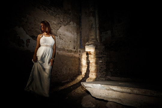Mujer con vestido blanco a contraluz en el templo antiguo iluminada por la luz del sol al atardecer