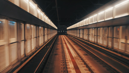 View of subway tunnel as seen from the rear window of moving train. Fast underground train departs from modern subway station.