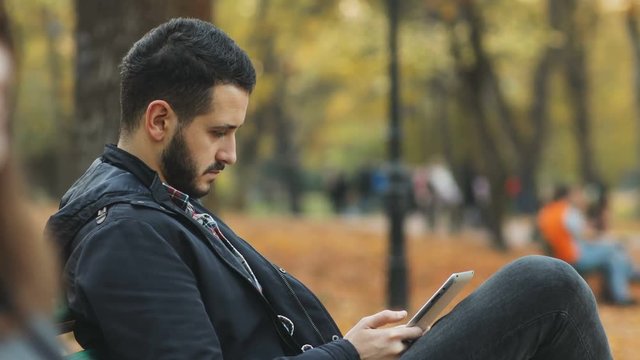 side view calm handsome bearded man holding modern tablet pc autumn park sitting bench online wifi technology user application notification download programm pda software update wireless gadget login