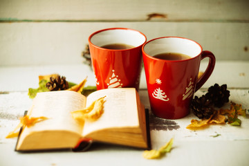 two red cups, wrapped in a scarf book and yellow leaves, autumn background, concept on the subject of comfort, warmth, pleasure, image toning