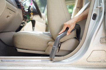 Close up hand of a man holding vacuum cleaner and cleaning inside a car
