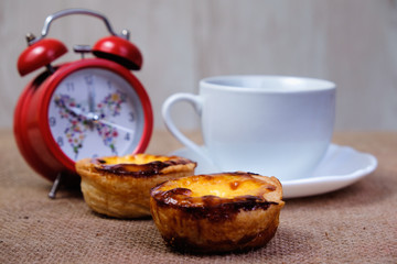 Obraz na płótnie Canvas Red alarm clock, cup of coffee and Portuguese Custard Tarts, called