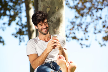 Fototapeta premium Smiling man sitting by tree barefoot with headphones and cellphone