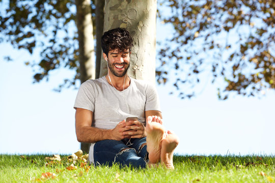Full body happy man sitting outside with mobile phone and headphones