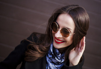 Naklejka premium young gorgeous woman in stylish sunglasses posing against brown wall background