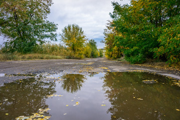 Fototapeta na wymiar Old road with puddles in the industrial area in autumn.