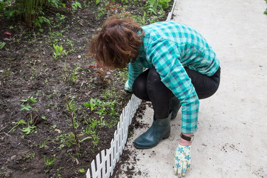 Woman Fixing A Decorative Fence On A Flower Bed