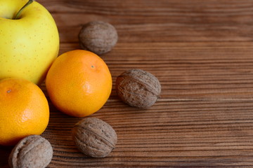 Fresh ripe mandarin, apple, walnuts on a wooden table. Organic sources of vitamins and minerals. Healthy nutrition. Brown wooden background with copy space for text