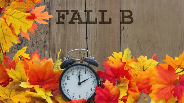 Fall Time Change, Autumn Leaves and Alarm Clock with grunge wood with text Fall Back 1 Hour