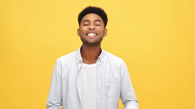 Smiling african man in shirt corrects his appearance and looking at the camera over yellow background