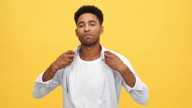Cool african man corrects his shirt and looking at the camera over yellow background