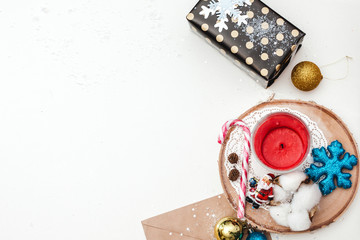Flat lay concept of Christmas items on a white table. Composition includes decorations, gifts, tableware, candle, lace, cotton, tree, snow, glitter, letter balloons and the figure of Santa Claus.