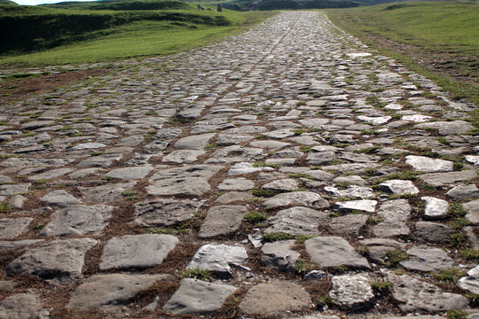 Ancient road paved with cobblestone and going up through hills.