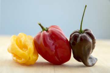Three habanero very hot chili peppers in a row, ripened capsicum chinenses on wooden table