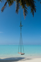 Tropical Paradise Maldives island with palms and blue sky, swinging on the wind. Swing hanging on a palm tree on Maldives. Beautiful tropical beach under cloudy sky with swing on coconut palm, Luxury.