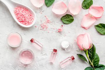 Products for skincare based on rose oil. Cream, lotion, spa salt on grey background top view