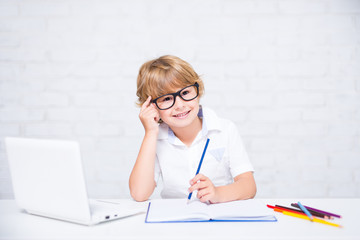 happy little school boy in glasses doing homework and thinking about something