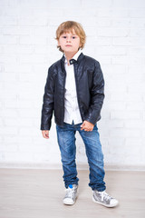 full length portrait of little boy in leather jacket posing over white brick wall