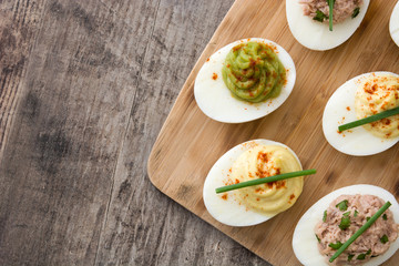 Variety of stuffed eggs with avocado and tuna  on wooden table.Top view - obrazy, fototapety, plakaty